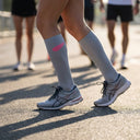 Runner wearing SA1NT LAYERS Compression Race Socks Light Grey Hot Pink at a race start line